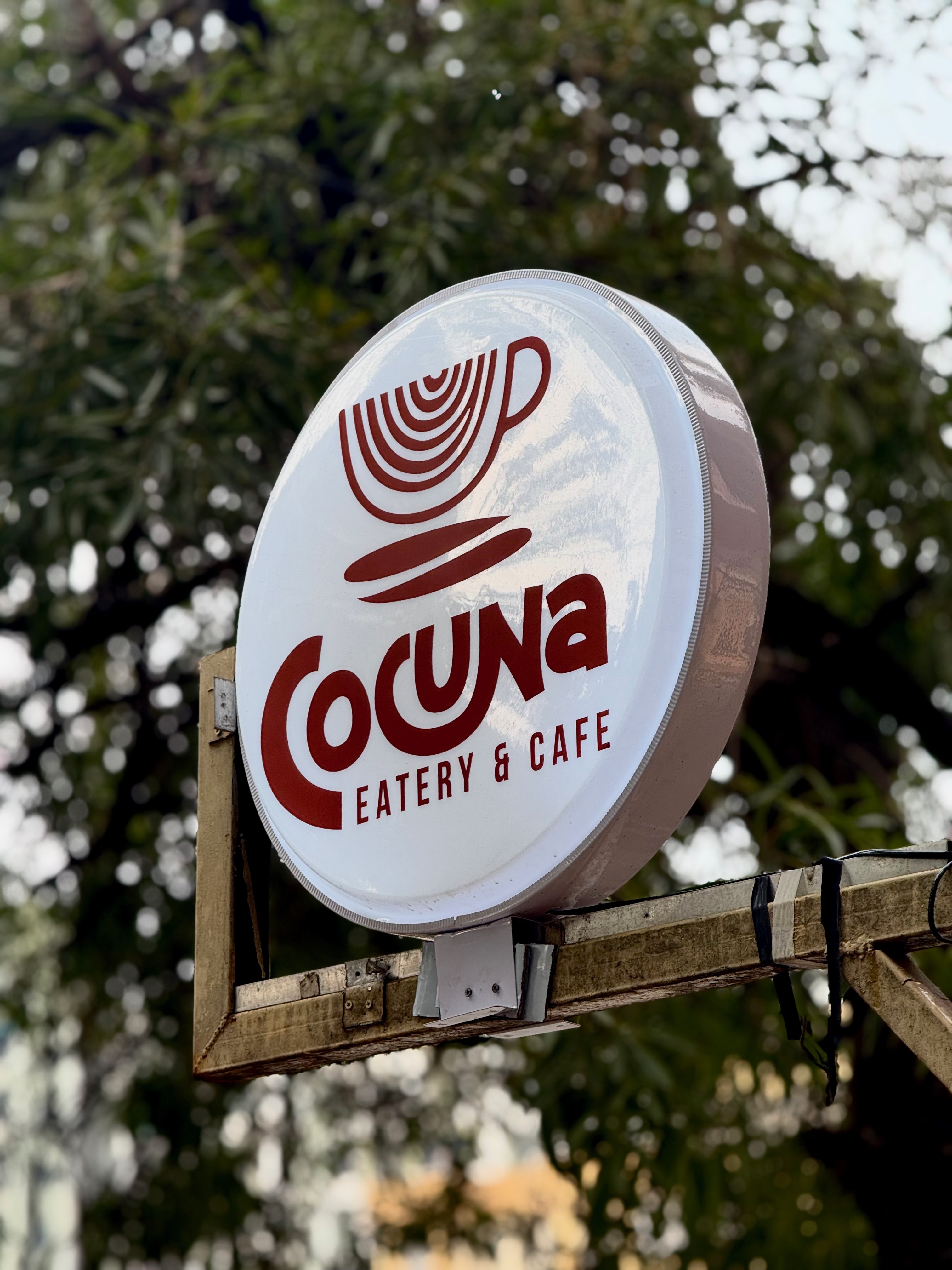 Cocuna’s round café sign beneath leafy trees